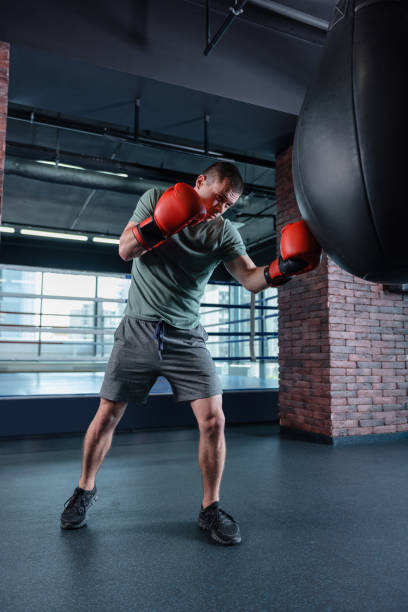 istock Dark-haired man wearing red boxing gloves training in gym 1002226518