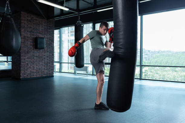 istock Dark-haired boxer beating punching bag with leg 1002238834