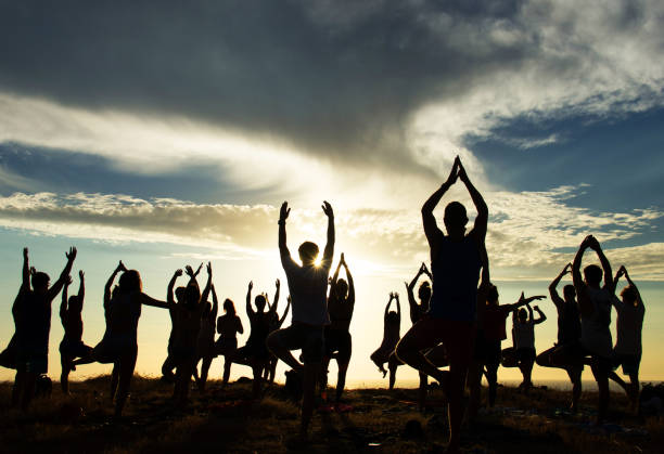 People Practicing Yoga at Sunset Silhouettes of people doing yoga on the beach at sunset group mountain silhouette stock pictures, royalty-free photos & images