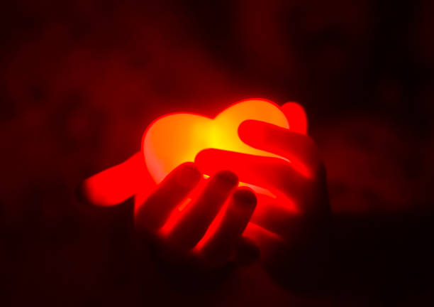 Human hands holding red glowing heart in the dark Human hands holding red glowing heart in the dark. passion stock pictures, royalty-free photos & images