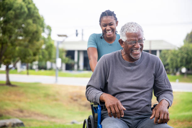 uomo di colore anziano in sedia a rotelle con figlia - senior adult wheelchair community family foto e immagini stock