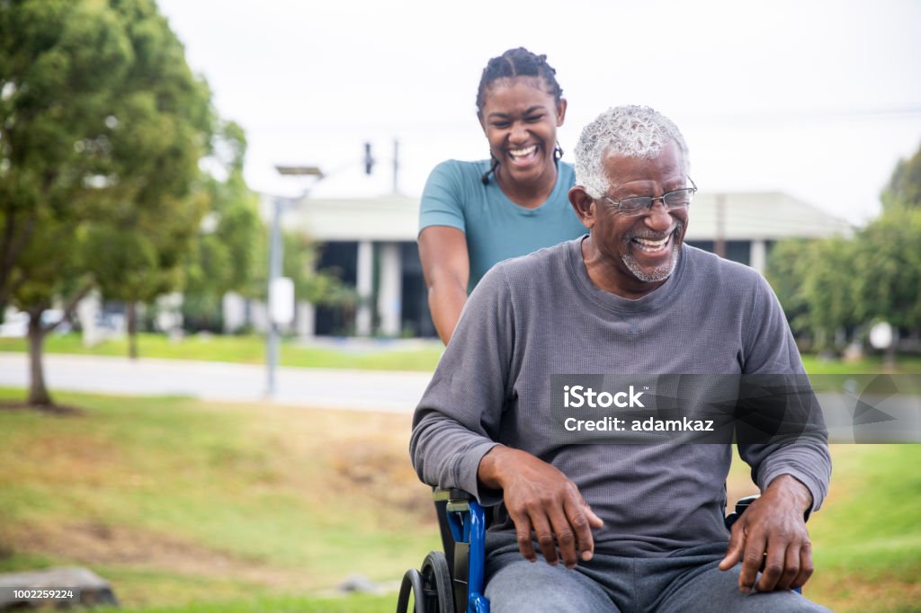 Senior black man in wheelchair with daughter A senior black man on a wheelchair is pushed around by his daughter after their basketball workout. Senior Adult Stock Photo