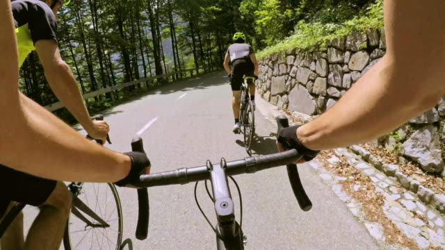 POV Road cyclist being overtaken by two male cyclists on the sunny mountain road