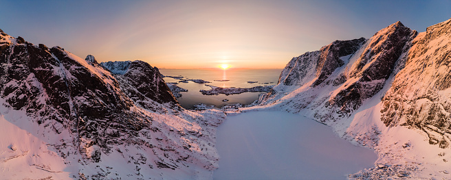Panorama aerial view of mountain range with ice lake in valley with arctic ocean at sunset. Reine, Lofoten islands, Norway