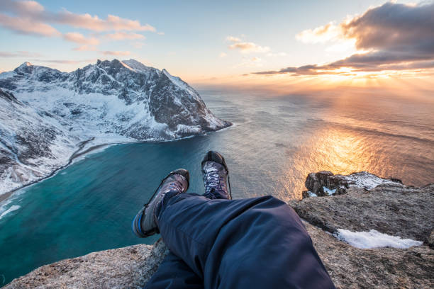istock Man hiker cross legs sitting on peak mountain with coastline at sunset 1002265146