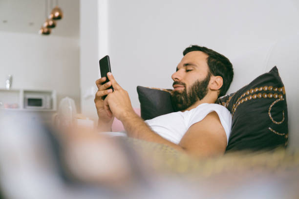 istock Young smiling single man using his smartphone on the bed 1002280822