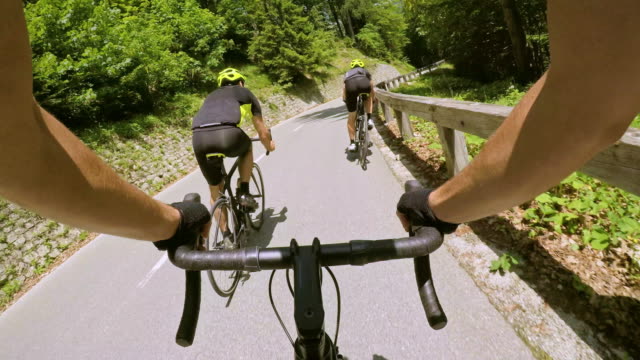 POV Road cycling with Two male cyclists down a mountain road in sunshine