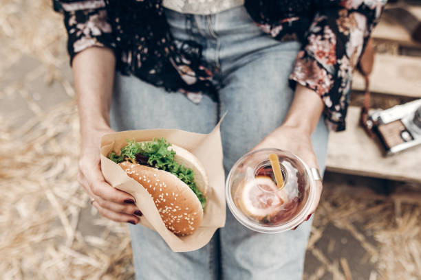 juicy burger and lemonade in hands, top view. stylish hipster woman holding  cheeseburger and refreshing drink. boho girl at street food festival. summer vacation picnic. space for text