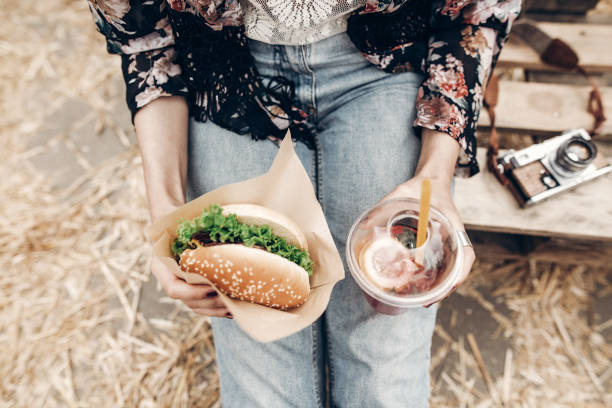 tasty burger and lemonade in hands, top view. stylish hipster woman holding juicy hamburger close up and refreshing cocktail. boho girl at street food festival. summertime
