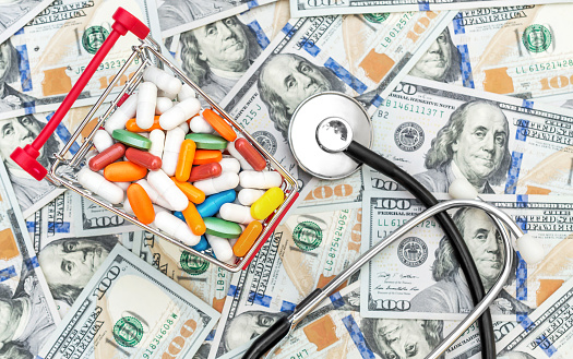 Full shopping cart with pills and stethoscope on background of dollar bills. Top view.