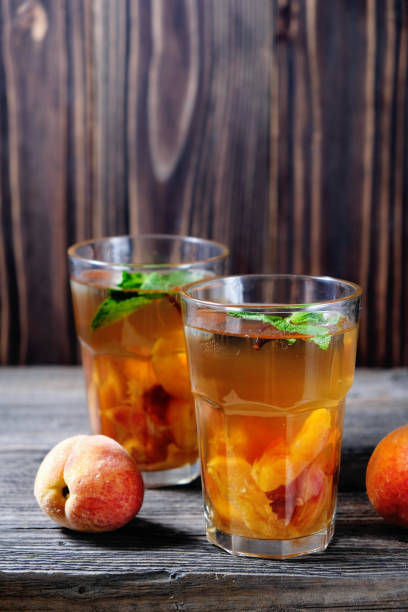 bevande fredde estive: sangria di pesca fatta in casa con cubetti di ghiaccio e menta in vetro su sfondo legno - peach nectarine wet drop foto e immagini stock