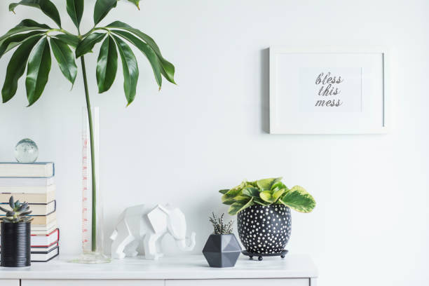 istock Scandinavian interior with white cupboard, mock up poster frame, elephant figures, tropical leaf, plants and books. Modern and minimalistic concept of space. 1002339876