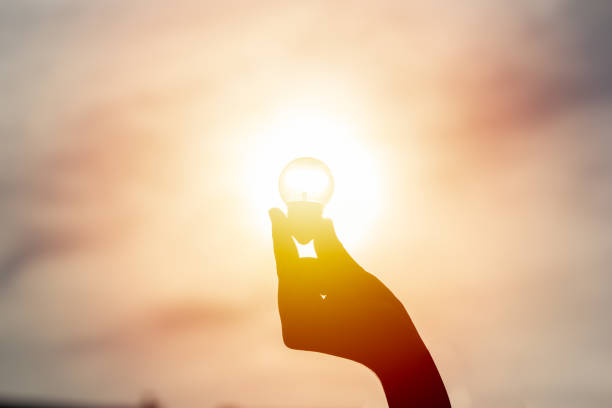 istock Idea and creativity concept. Silhouette hand holding light bulb with solar energy. New ideas innovation concept. Conceptual solar energy sustainable. Energy savings. 1002342622