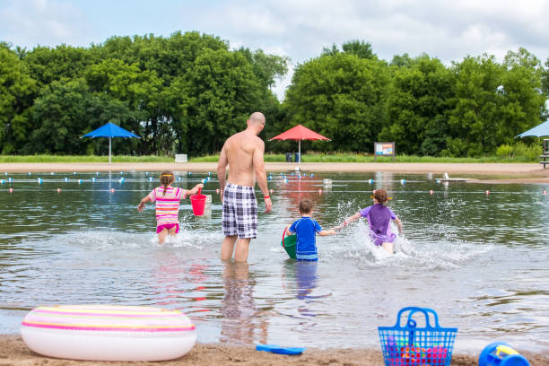 istock Father & Three Young Children Playing in Water at Beach 1002376130