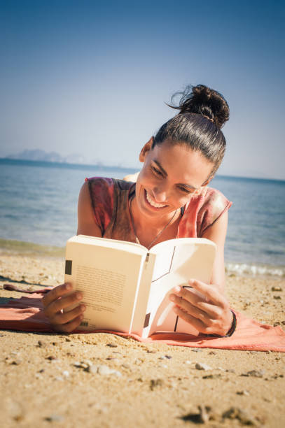 istock Woman reading book while enjoying the sunshine at the beach 1002395840