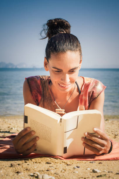 istock Woman reading book while enjoying the sunshine at the beach 1002405444