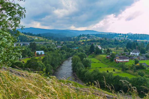 istock an exciting landscape on a mountain river with willows along the shores and a town on both sides of the stream against the background of the distant blue mountains 1002410180