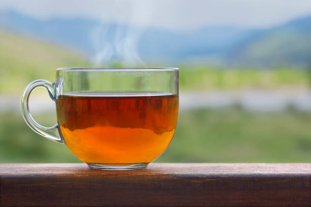 Transparent cup of black hot tea on a wooden table on a background of nature