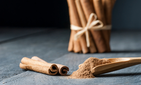 Close up cinnamon sticks and powder healthy spice on black wooden background