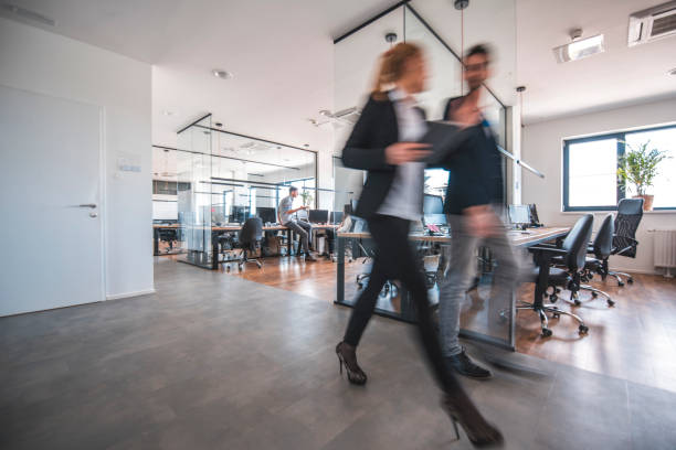 Colleagues discussing while walking in office Businesswoman discussing with male colleague while walking in office. Male and female web designers are communicating at workplace. They are wearing smart casuals. incidental people stock pictures, royalty-free photos & images