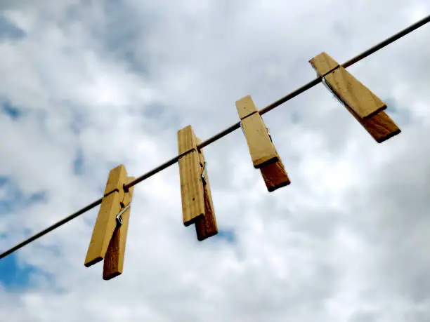 A line of four wooden clothes pegs on hanging from a clothes drying line outdoors. With a background of a cloudy blue sky on a breezy summers day