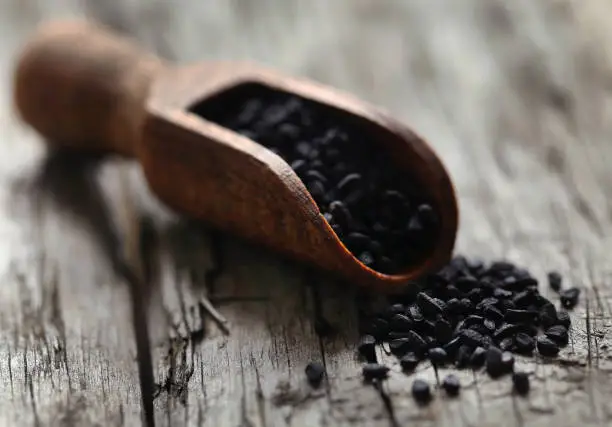 Nigella seeds in wooden scoop on timber surface