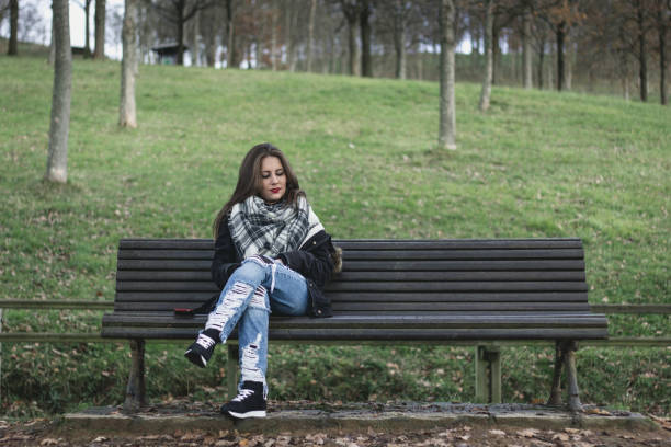 istock Young woman sitting on park bench looking down to space next to her 1002493616