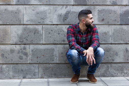 Bearded hipster wearing blue jeans and checkers flannel shirt on the street over grey background