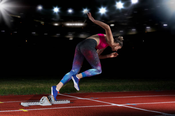 istock woman sprinter leaving starting blocks on the athletic track. exploding start on stadium with reflectors 1002511904