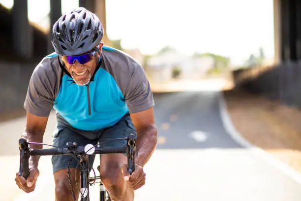 A senior black man sprints on his road bike training for a race.