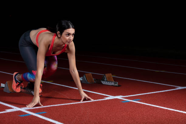 istock woman sprinter leaving starting blocks on the athletic track. exploding start on stadium with reflectors 1002514586