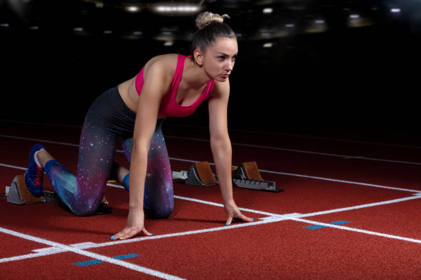 istock woman sprinter leaving starting blocks on the athletic track. exploding start on stadium with reflectors 1002515686