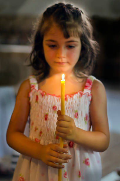 A child holds a candle in hands, focus on candle