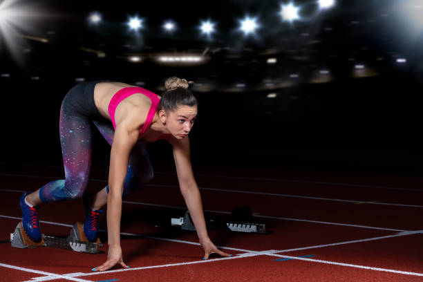 istock woman sprinter leaving starting blocks on the athletic track. exploding start on stadium with reflectors 1002537776