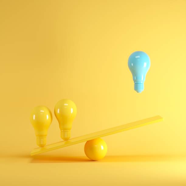istock Outstanding Blue light bulb floating between yellow lightbulbs on yellow seesaw, minimal idea concept. 1002547004