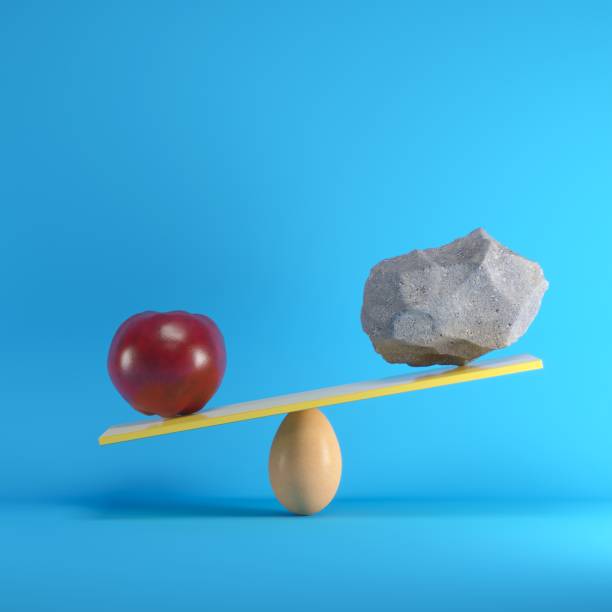 istock Red Apple and Rock playing on yellow seesaw on blue background. Minimal idea concept. 1002547018