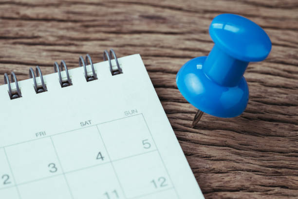 予定、締め切り、休日や日付の計画コンセプトや大きな青いプッシュピン画鋲ピン白クリーン カレンダーの横にある木のテーブル - calendar deadline personal organizer thumbtack ストックフォトと画像