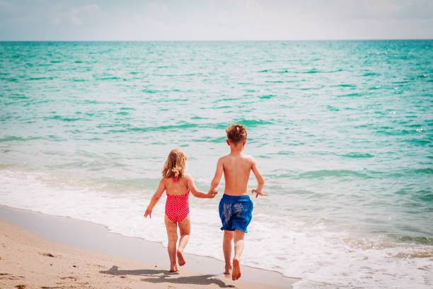 istock little boy and girl run play at beach 1002561048
