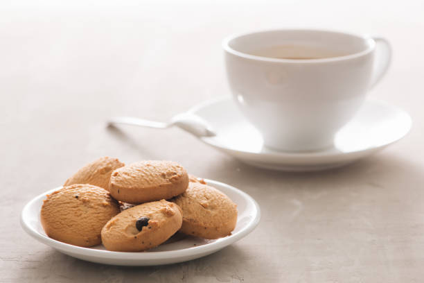 istock Coffee. White porcelain cup of freshly brewed coffee top view close-up arranged with  biscuits, spoon and plate on light background 1002595546