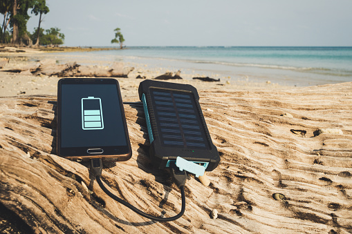 Alternative energy source. battery is charged by solar energy. Charging mobile devices in the wild. island beach. Powerbank charges the phone on the background of palm trees and sandy beach