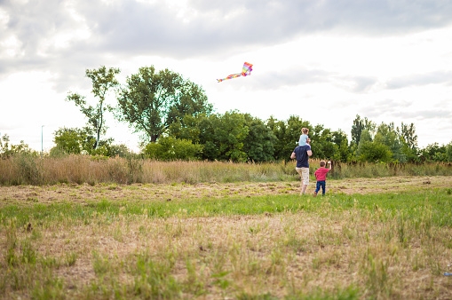 Father, a boy and a girl are running kite on the field.