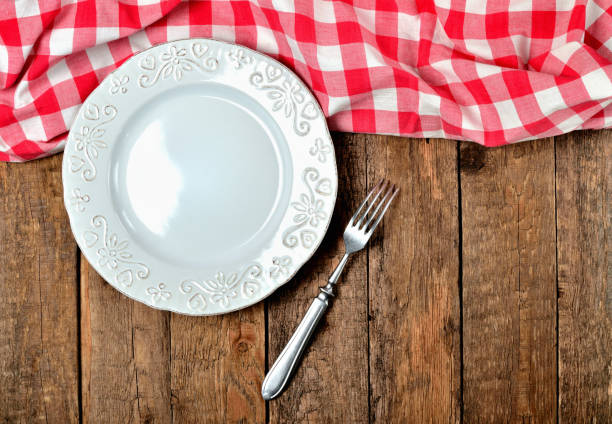 istock Decorative ceramic plate, fork and red checkered tablecloth on top side on old vintage wooden table background - top view 1002631422