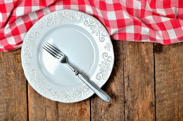 istock Fork in white decorative ceramic plate and red checkered tablecloth on top side on old vintage wooden table background - view from above 1002634966