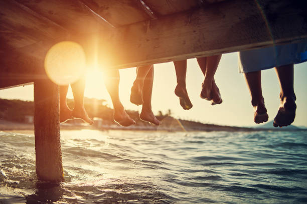 familie zittend op pier door de zee - strand fotos stockfoto's en -beelden