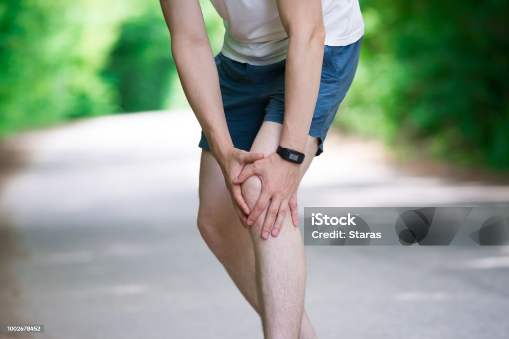 Pain in knee, joint inflammation, massage of male leg, injury while running, trauma during workout Pain in knee, joint inflammation, massage of male leg, injury while running, trauma during workout, outdoors concept Adult Stock Photo