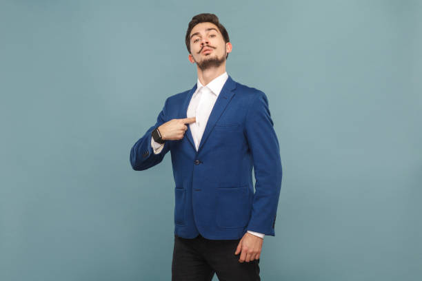 Proud man pointing finger himself Proud man pointing finger himself. portrait of handsome bearded businessman in blue suit and white shirt, with smart watch. Indoor studio shot, isolated on light blue background egocentric stock pictures, royalty-free photos & images