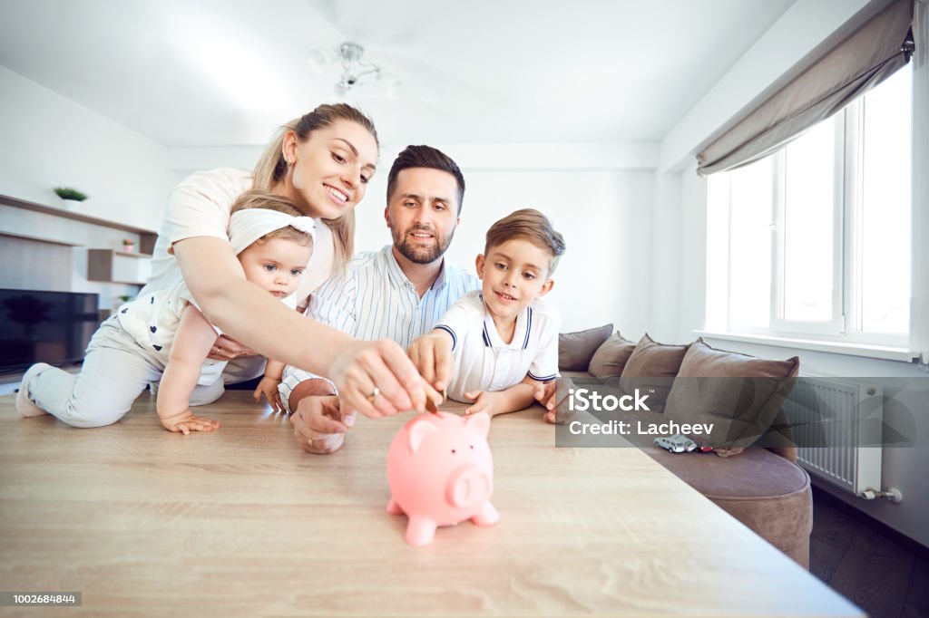 Una famiglia sorridente risparmia denaro con un salvadanaio - Foto stock royalty-free di Famiglia