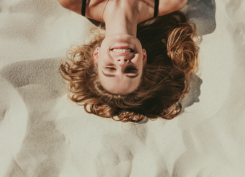 Close up top view of a smiling woman lying on beach sand. Close up of head and shoulders of a woman with closed eyes relaxing on beach.