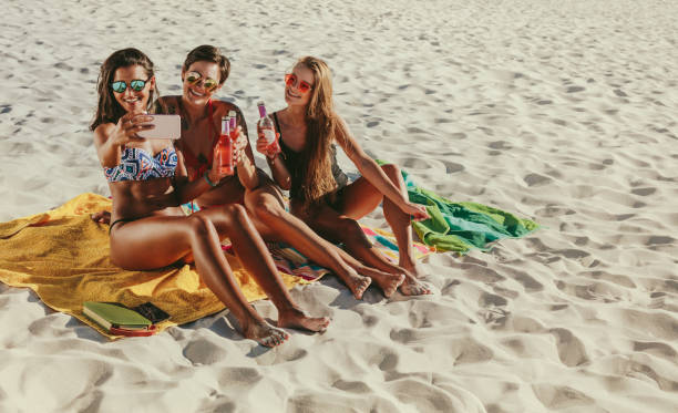 istock Women sitting at the beach taking a selfie 1002688378