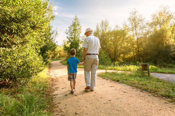 Grandfather and grandchild walking outdoors Back view of grandfather with hat and grandchild walking on a nature path grandson photos stock pictures, royalty-free photos & images